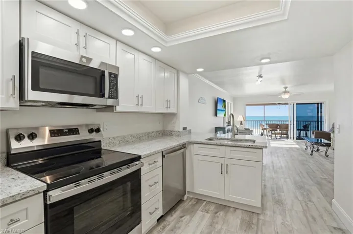 Kitchen with stainless steel appliances, open floor plan, white cabinetry, ornamental molding, and light wood-type flooring - Virtually Edited Image