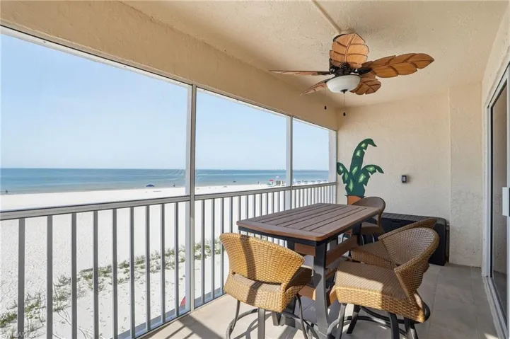 Sunroom / solarium with ceiling fan, view of water and beach, and a balcony - Virtually Edited Image