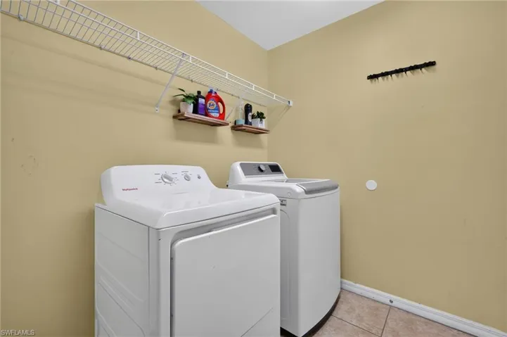 Dedicated utility space featuring a white top-load washer and dryer set, wire shelving, and tile flooring
