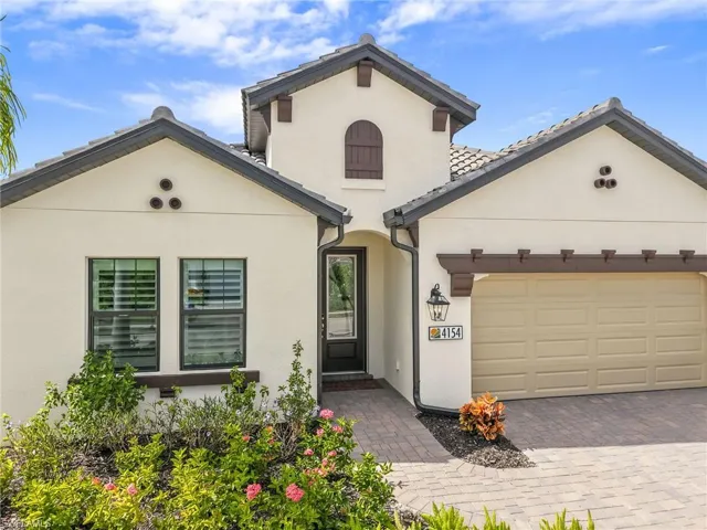 Stucco exterior featuring decorative corbels, multi-gabled roofline, paver driveway, arched architectural accent, and glass-paneled front door