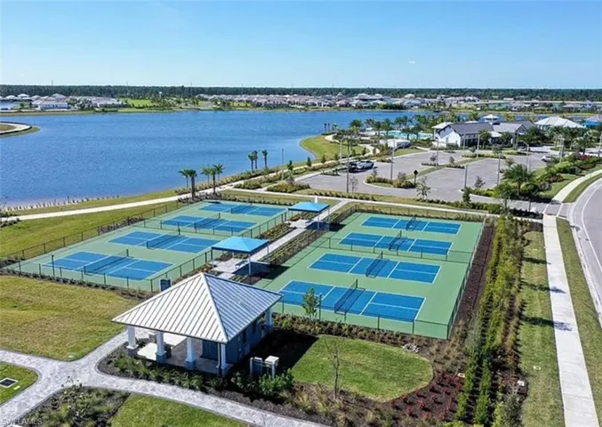 Recreational complex featuring multiple fenced tennis courts, shaded seating pavilions, paved walkways, and direct lakefront positioning