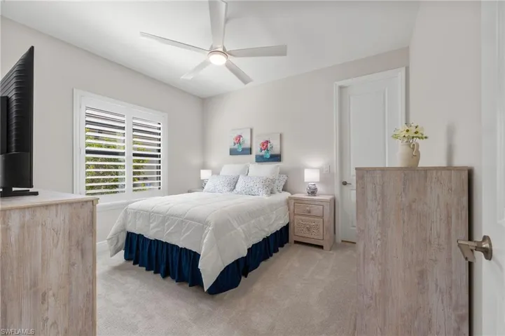 Neutral wall tones, carpeted flooring, white plantation shutters, and a central ceiling fan with integrated lighting