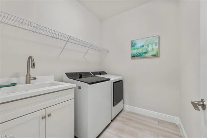 Laundry room featuring wood-finish flooring, a white vanity cabinet with a stone countertop, an integrated sink with a high-arch pull-down faucet, and overhead wire shelving