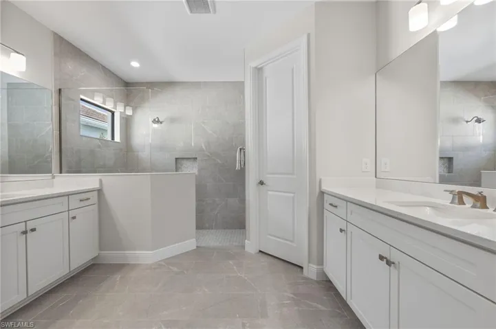 Dual vanity featuring white shaker-style cabinetry, solid-surface countertops, and wall-to-wall mirrors, paired with a walk-in shower finished in floor-to-ceiling neutral tile