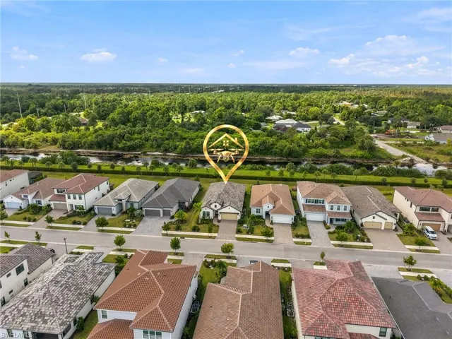 Aerial perspective of a single-story residence featuring a multi-gabled roofline, light-colored stucco exterior, two-car garage, paved driveway, and direct frontage to a canal and wooded perimeter