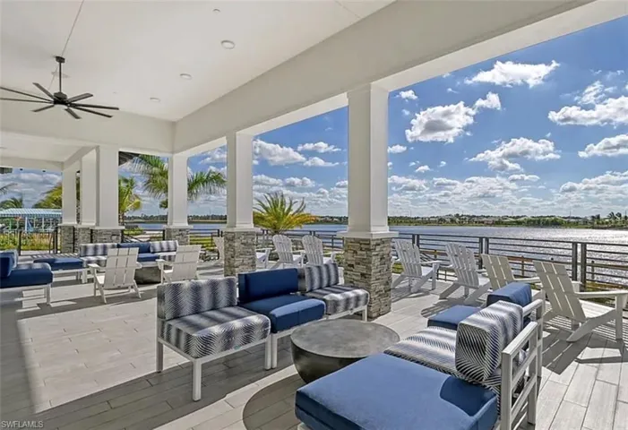 Covered porchfeaturing tile flooring, stone-accented columns, a ceiling fan, and metal railings overlooking the water