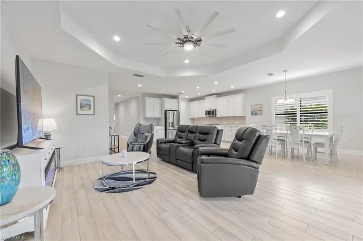 Open-concept interior featuring wood-finish tile flooring, a tray ceiling, recessed lighting, and a multi-blade ceiling fan