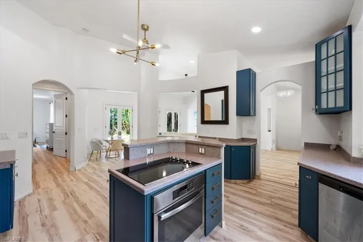 Kitchen featuring blue cabinets, arched walkways, a chandelier, and a towering ceiling