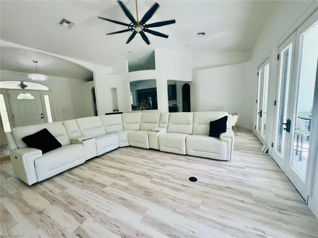 Living area with french doors, arched walkways, light wood-style flooring, a ceiling fan, and high vaulted ceiling