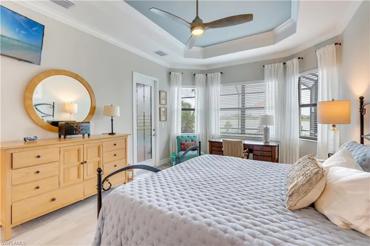 Bedroom featuring ceiling fan, multiple windows, a tray ceiling, and crown molding