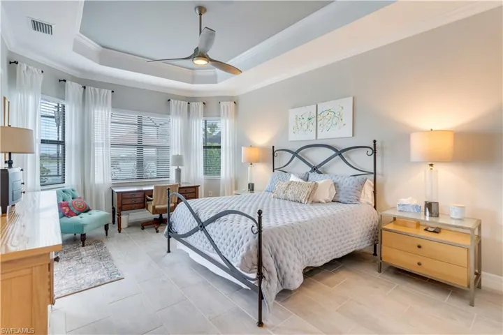 Bedroom with ceiling fan, a tray ceiling, light tile flooring, and ornamental molding