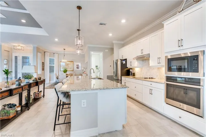Kitchen with light stone countertops, black appliances, sink, a kitchen island with sink, and white cabinetry