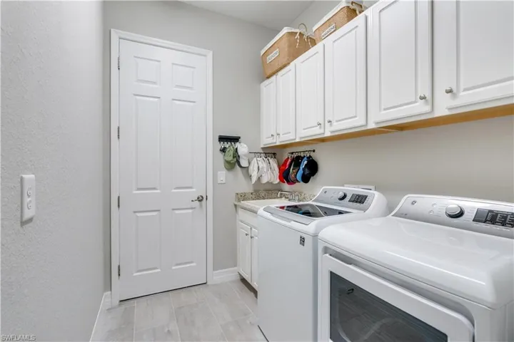 Laundry room featuring separate washer and dryer, light tile flooring, sink, and cabinets