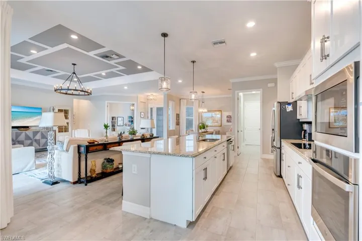 Kitchen featuring light stone counters, a center island with sink, hanging light fixtures, white cabinets, and sink