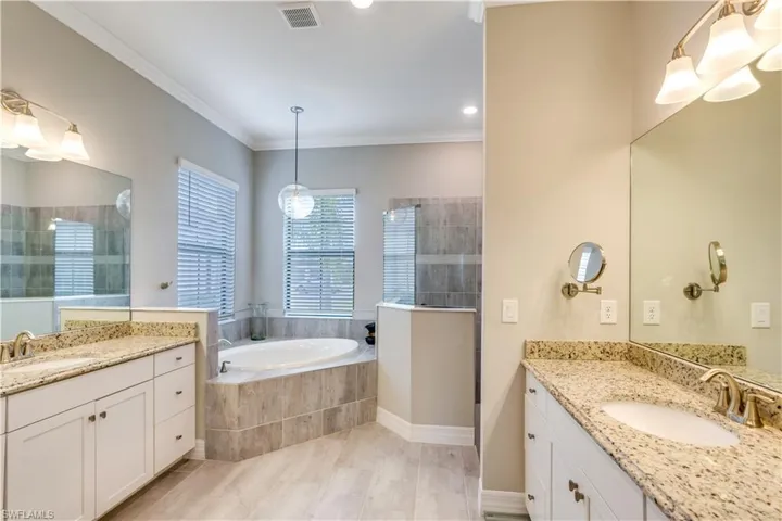 Bathroom with oversized vanity, crown molding, and tiled tub