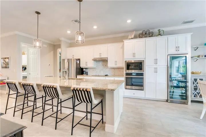 Kitchen with white cabinetry, hanging light fixtures, stainless steel appliances, an island with sink, and a breakfast bar