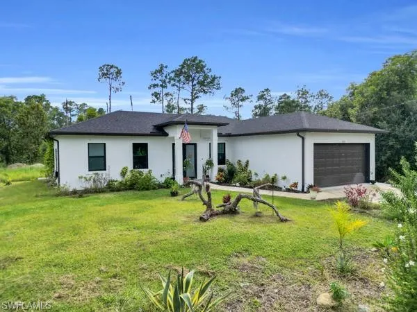 View of front of house with an attached garage, stucco siding, a front lawn, and roof with shingles
