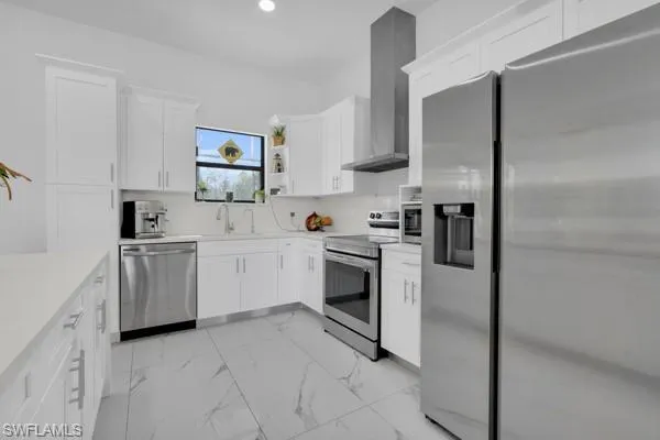 Kitchen with stainless steel appliances, white cabinetry, light marble finish floors, backsplash, and wall chimney range hood
