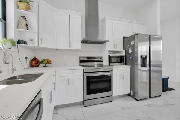 Kitchen with stainless steel appliances, white cabinetry, wall chimney range hood, and open shelves