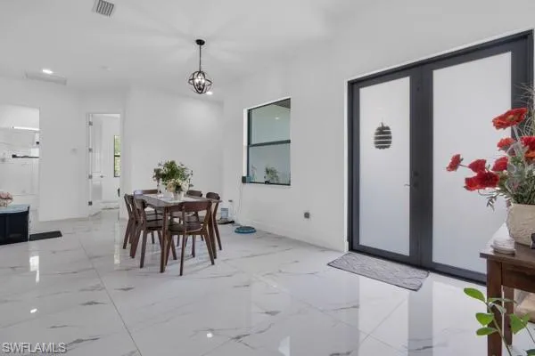 Dining space featuring french doors, light marble finish flooring, recessed lighting, and a chandelier