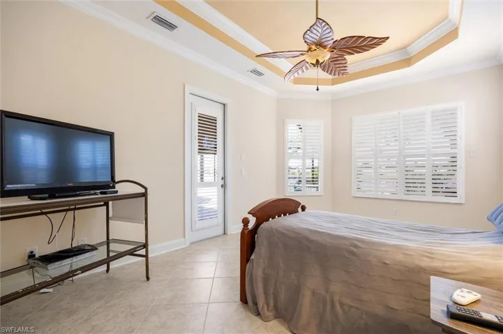 Bedroom with crown molding, a ceiling fan, a raised ceiling, and light tile patterned floors