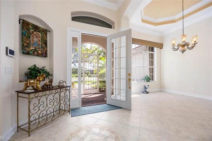 Entrance foyer with crown molding, light tile patterned floors, suspended lighting, french doors, and a raised ceiling