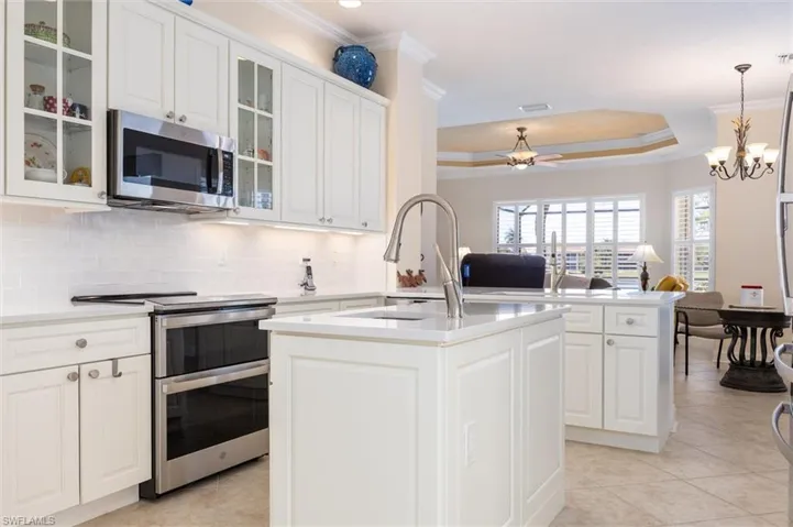Kitchen with stainless steel appliances, a kitchen island with sink, open floor plan, light tile patterned floors, and ornamental molding