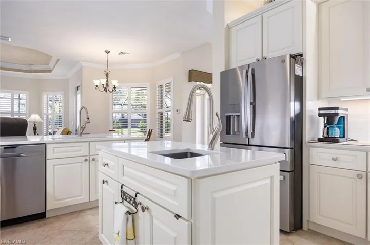 Kitchen featuring stainless steel appliances, light stone counters, white cabinetry, an island with sink, and suspended lighting