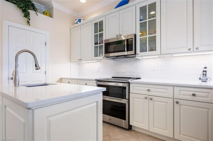Kitchen featuring stainless steel appliances, white cabinetry, light stone countertops, glass insert cabinets, and crown molding
