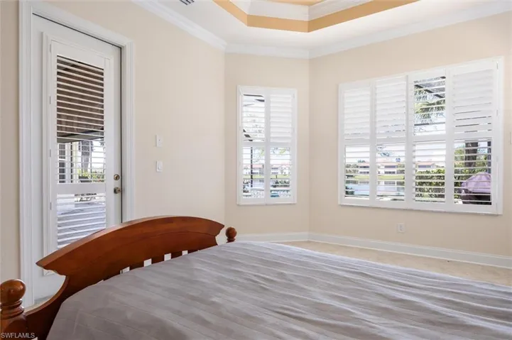 Bedroom with ornamental molding, multiple windows, a tray ceiling, light colored carpet, and access to outside