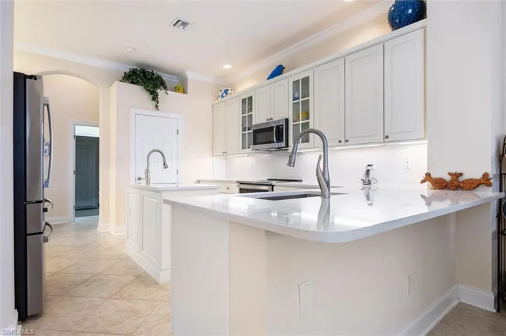 Kitchen with white cabinetry, a peninsula, glass insert cabinets, stainless steel appliances, and light stone countertops