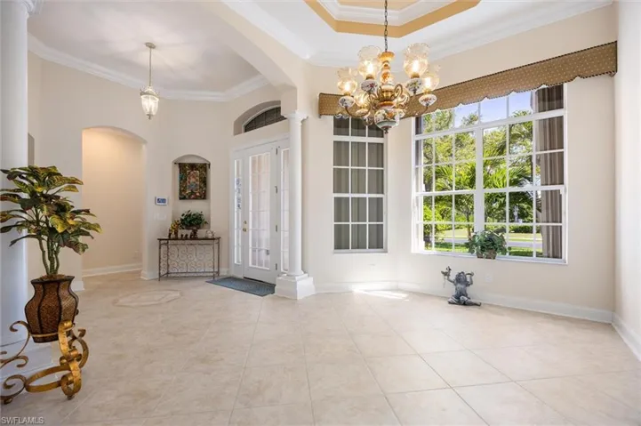 Foyer with ornamental molding, arched walkways, a high tray ceiling, hanging lights, and light tile patterned floors