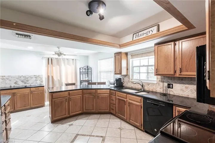 Kitchen with tasteful backsplash, dark countertops, light tile patterned flooring, black dishwasher, and a ceiling fan