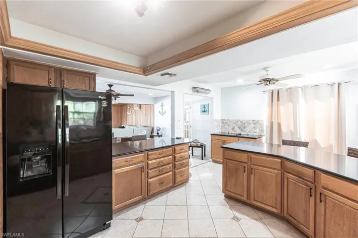 Kitchen featuring black refrigerator with ice dispenser, dark countertops, a ceiling fan, brown cabinets, and light tile patterned floors