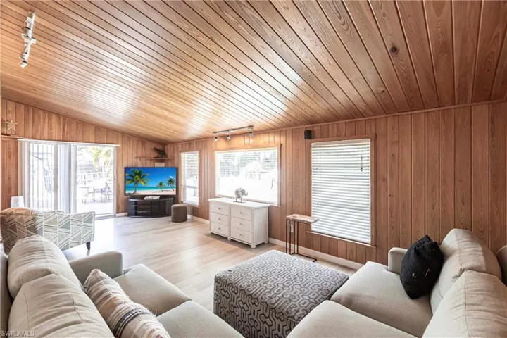 Living room with rail lighting, wood finished floors, wooden ceiling, lofted ceiling, and wood walls