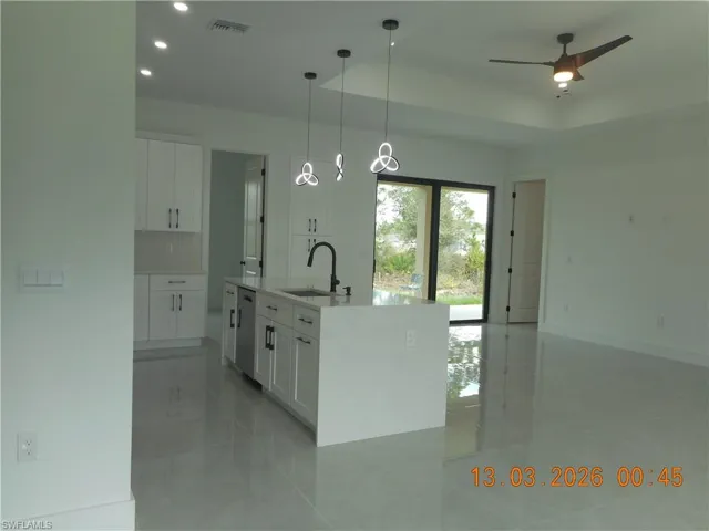 Kitchen featuring white cabinetry, an island with sink, light stone counters, hanging light fixtures, and a ceiling fan