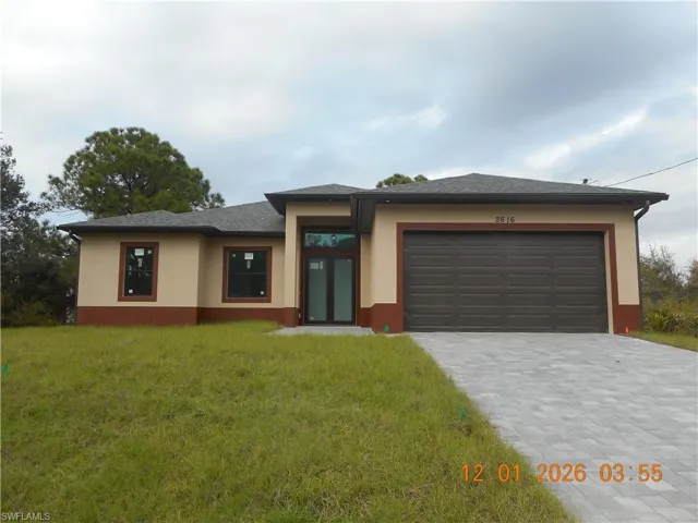 Prairie-style house with decorative driveway, stucco siding, a front yard, and an attached garage