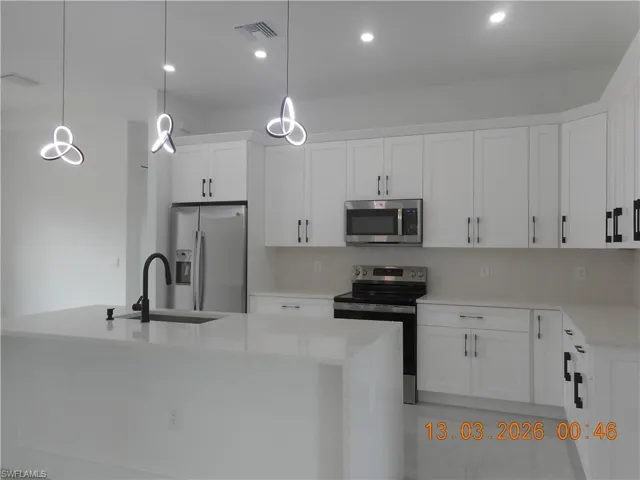 Kitchen featuring stainless steel appliances, light stone countertops, white cabinets, and a kitchen island with sink