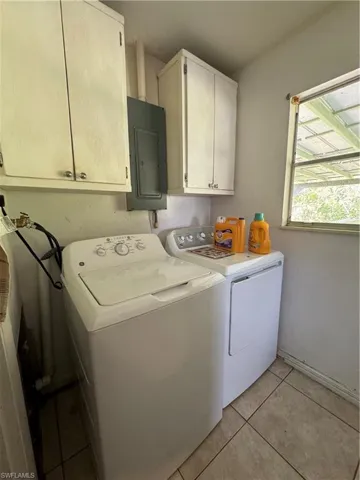 Washroom featuring electric panel, cabinets, washing machine and clothes dryer, and light tile patterned floors