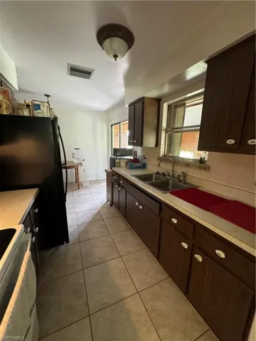 Kitchen featuring light tile patterned flooring, range, dark brown cabinets, decorative backsplash, and sink