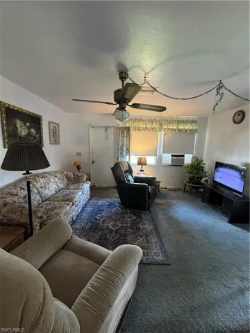 Living room featuring ceiling fan, a textured ceiling, and dark carpet