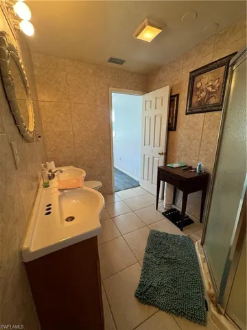 Bathroom with tile walls, tile patterned flooring, vanity, and a shower with door