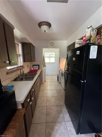 Kitchen featuring sink, light tile patterned flooring, backsplash, dark brown cabinets, and fridge