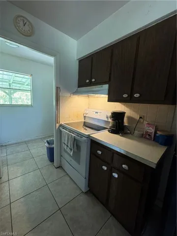 Kitchen with decorative backsplash, dark brown cabinetry, range, light tile patterned flooring, and range hood