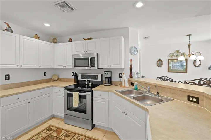 Kitchen with white cabinets, hanging light fixtures, appliances with stainless steel finishes, sink, and light tile floors