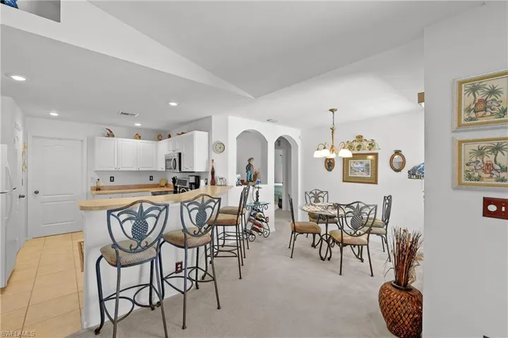 Kitchen with kitchen peninsula, pendant lighting, light colored carpet, a kitchen bar, and white cabinetry