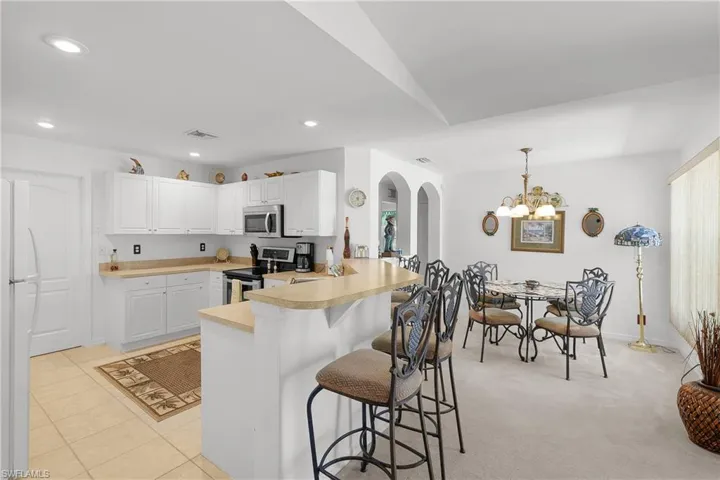 Kitchen featuring decorative light fixtures, kitchen peninsula, a kitchen breakfast bar, light colored carpet, and appliances with stainless steel finishes