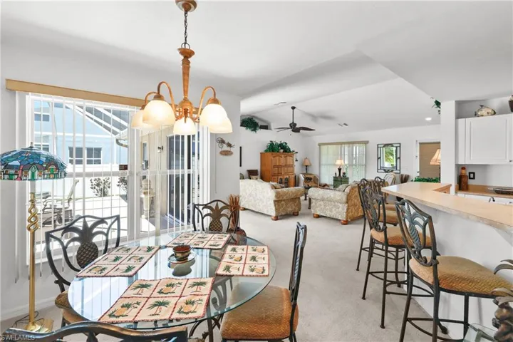 Carpeted dining space featuring ceiling fan with notable chandelier and a wealth of natural light