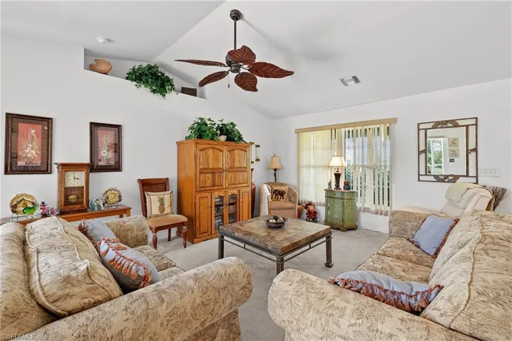 Living room featuring high vaulted ceiling, ceiling fan, and light carpet