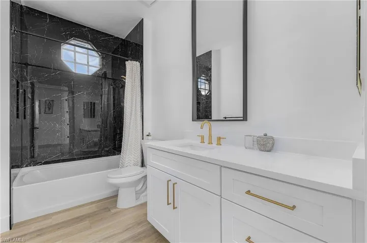 Full bathroom with hardwood / wood-style flooring, shower / tub combo with curtain, vanity, and toilet
